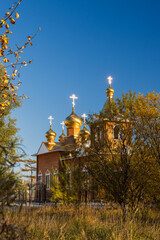 View of the building of the Orthodox Church and autumn bushes with yellow foliage. Crosses glitter in the sun. Christianity in Siberia. Ola urban-type settlement, Magadan region, Far East of Russia.
