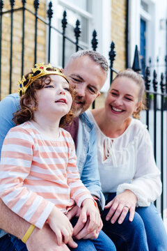 Family Sitting On Front Porch Stairs And Playing With A Toy Crown.