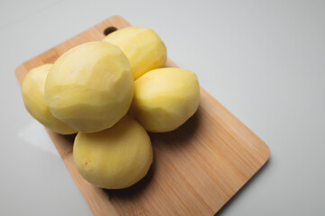 peeled potatoes lie on a wooden cutting board in a pile, close-up