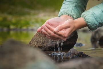 Close-up of water drops falling from female hands into a stream. The hand touches fresh water. A tourist drinks water from a reservoir in the mountains in summer on a sunny day