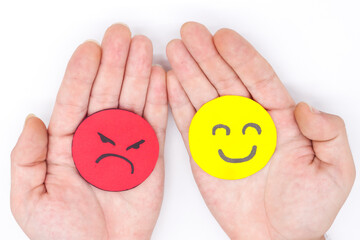 hands holding two angry and happy faces of yellow and red paper on a white background. Concept of...