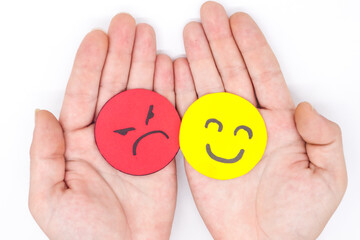 hands holding two angry and happy faces of yellow and red paper on a white background. Concept of...