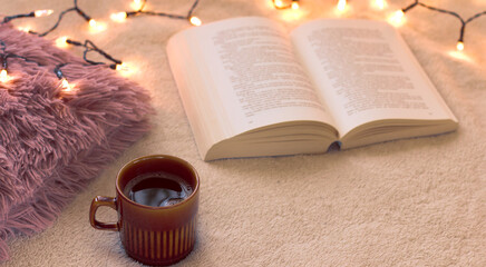 Concept of relaxation and hygge on a winter day. A cup of black, hot coffee and an open book on the...