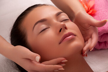 Obraz na płótnie Canvas Beautiful caucasian woman enjoying facial massage with closed eyes in sunny spa salon. Relaxing treatment in medicine