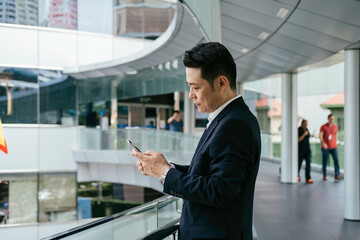 Side View Of A Serious Asian Businessman Using A Mobile Phone At Office Balcony