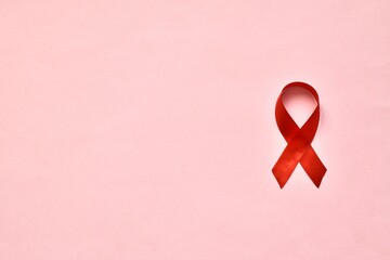 Red ribbon on a pink background. The symbol of The World AIDS Day or cancer or HIV Awareness Month....