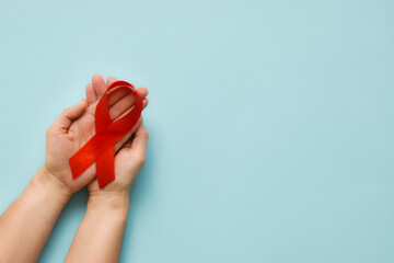 Healthcare and medicine concept - female hands holding red AIDS awareness ribbon on blue...