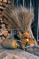 
Rustic composition with a bouquet of dried flowers, a broom and pumpkin on the background of a pile of firewood.