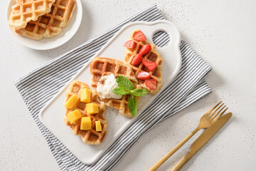 Tasty breakfast with mango, strawberries, sour cream on white background. Croissant as waffle. View from above.