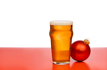 Pint glass of ale or beer with christmas bauble on red background