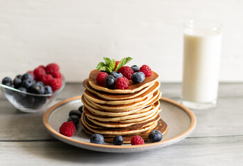 Pancakes with raspberries, blueberries, mint and milk on a light background