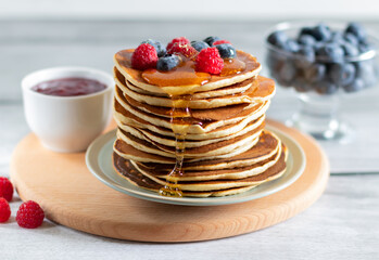 Pancakes with raspberries, blueberries, jam and trickle of honey on wooden board