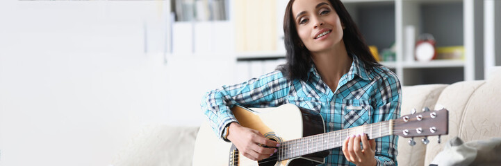Pretty brunette woman playing on guitar in living room, female spend free time to learn new hobby