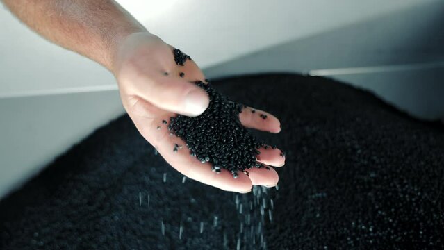 A man collects rubber granules with his hand, close-up. Raw material for production of rubber products.