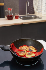 Cropped close-up shot of a heart shaped pancakes made in a red silicone mold in a frying pan in the kitchen across from the sink. Pancakes are in a silicone heart shaped mold. Top view.
