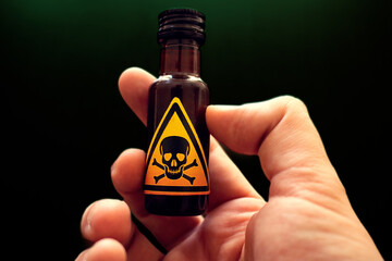 hand holding a small bottle of poison with a yellow toxic sign represented by a skull and two bones...