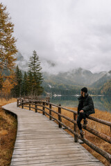 Eine Junge Frau sitzt auf einem Holzgeländer am Antholzer See in den Dolomiten. Herbst