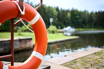 Red orange lifebuoy selective focus on summer green nature background with boat river channel and...