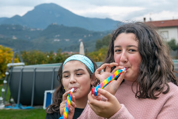Two young girls celebrating and playing with blower whistles at a house party