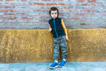 child in hooded sweatshirt and camouflage pants leaning against brick wall