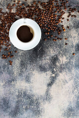 white cup of fresh brewed coffee and much roasted coffee beans on an old background with chocolate