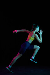 Dynamic portrait of young sportive woman training, running isolated on dark background in neon light. Competition, sport, fitness, speed and energy concept.