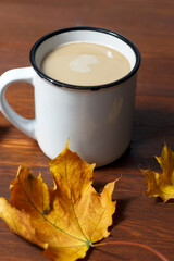 cup of coffee with milk and yellow autumn leaves on brown background