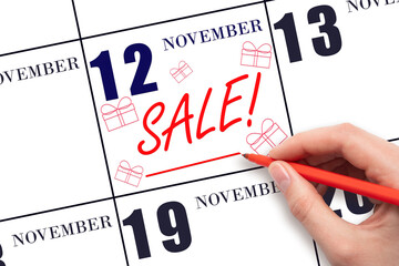 Hand writing text SALE and drawing gift boxes on calendar date November 12. Shopping Reminder