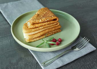 Lingonberry pancakes on a green plate with a fork and napkin. The concept is a dish of different peoples of the world.