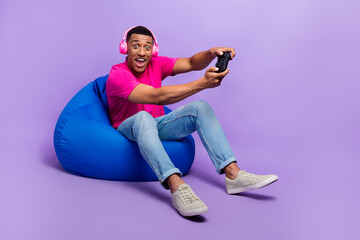 Photo of positive astonished man addicted user gamer wear stylish clothes sit comfort chair have fun isolated on purple color background © deagreez