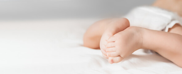 The baby crawls on a white bed. Legs of a newborn look straight