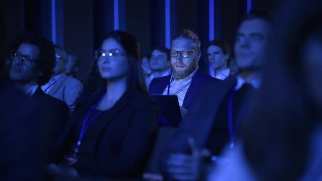 Male Sitting in a Dark Crowded Auditorium at an International Conference. Professional Using Laptop Computer. Innovative Presentation Concept: Technology, Science, Health, Mindfulness, Business.