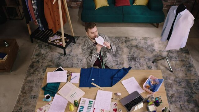 A man throws a paper airplane up high at the ceiling and then gets back to work as he is bopping his head to the music while measuring out fabric