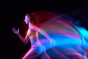 Energy. Professional female athlete, runner in motion over dark background in mixed neon light....