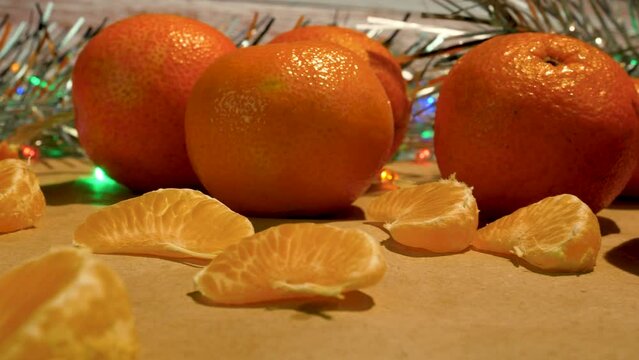 Orange large tangerines and slices of tangerines on the table against the backdrop of Christmas lights and shiny New Year's tinsel. Sweet treats for Christmas