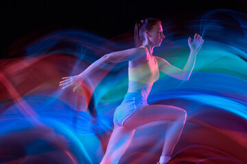 Glow. Professional female athlete, runner in motion over dark background in mixed neon light. Art, beauty, sport, cyberpunk concept