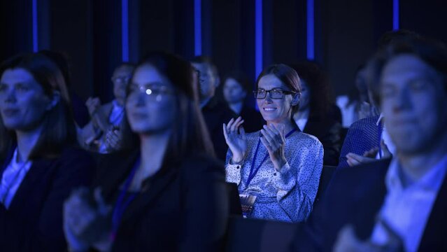 Beautiful Female Sitting in a Dark Crowded Auditorium at a Conference. Young Woman Clapping After a Successful Keynote Presentation. Specialist Inspired by Latest Technology. Slow Motion Footage.