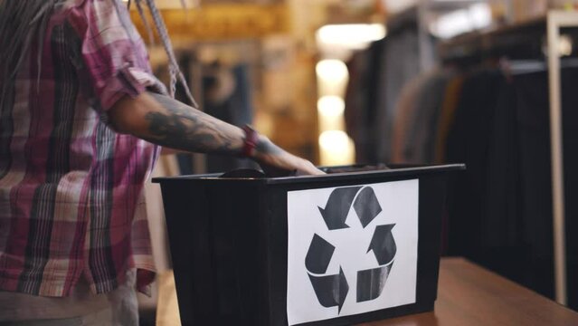Cropped shot of people putting clothes in container with recycle sign. Realtime
