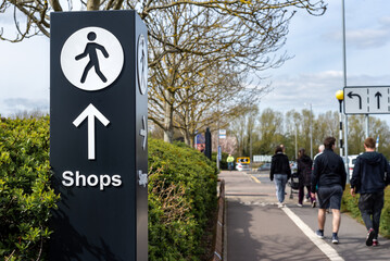 Multidirectional wayfinding sign with arrow and person walking icon pointing towards shops. 