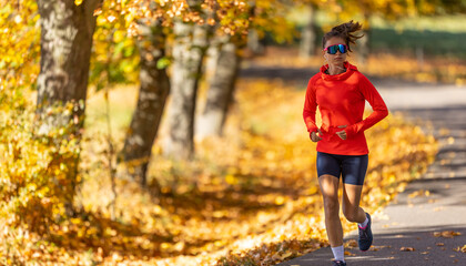 Fototapeta premium Young female athlete in sportswear runs in the park during warm indian summer