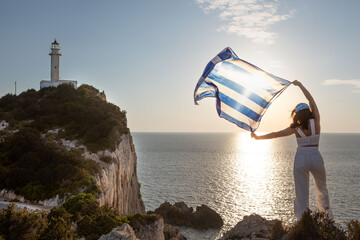 woman with greece flag looking at sunset above the sea