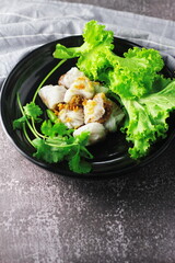 Thai Steamed Pork Dumplings served in a black plate with lettuce and coriander in a restaurant in Thailand.