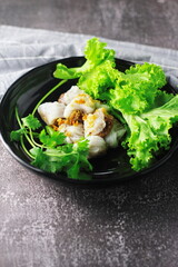 Thai Steamed Pork Dumplings served in a black plate with lettuce and coriander in a restaurant in Thailand.