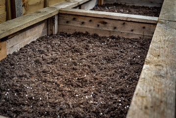 Closeup of big wooden planter vegetable box container in garden filled with soil ready for planting seeds and plants.