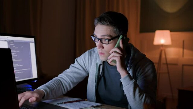 busy male freelancer works multitasking on laptop in home office because of burning deadlines, types on laptop keyboard, answer calls. young focused student on distance education makes notes. 