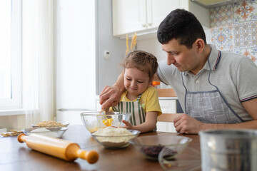 happy child helping to father in kitchen. kid cooking food with dad. little girl, man in apron in preparing dough, baking pie, cookies, making biscuit. family together home