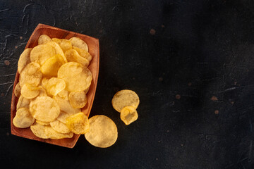 Obraz na płótnie Canvas Potato chips or crisps in a bowl, shot from above on a black background with a place for text