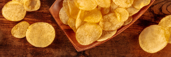 Potato chips or crisps, a salty snack on a wooden background, a panoramic header, top shot