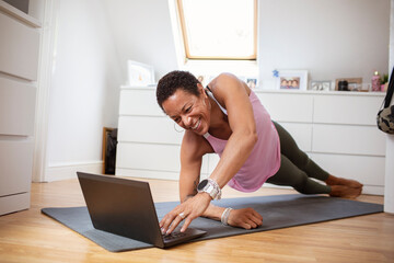 Happy mature woman exercising at laptop on yoga mat
