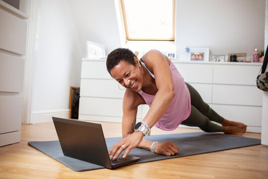 Happy mature woman exercising at laptop on yoga mat
